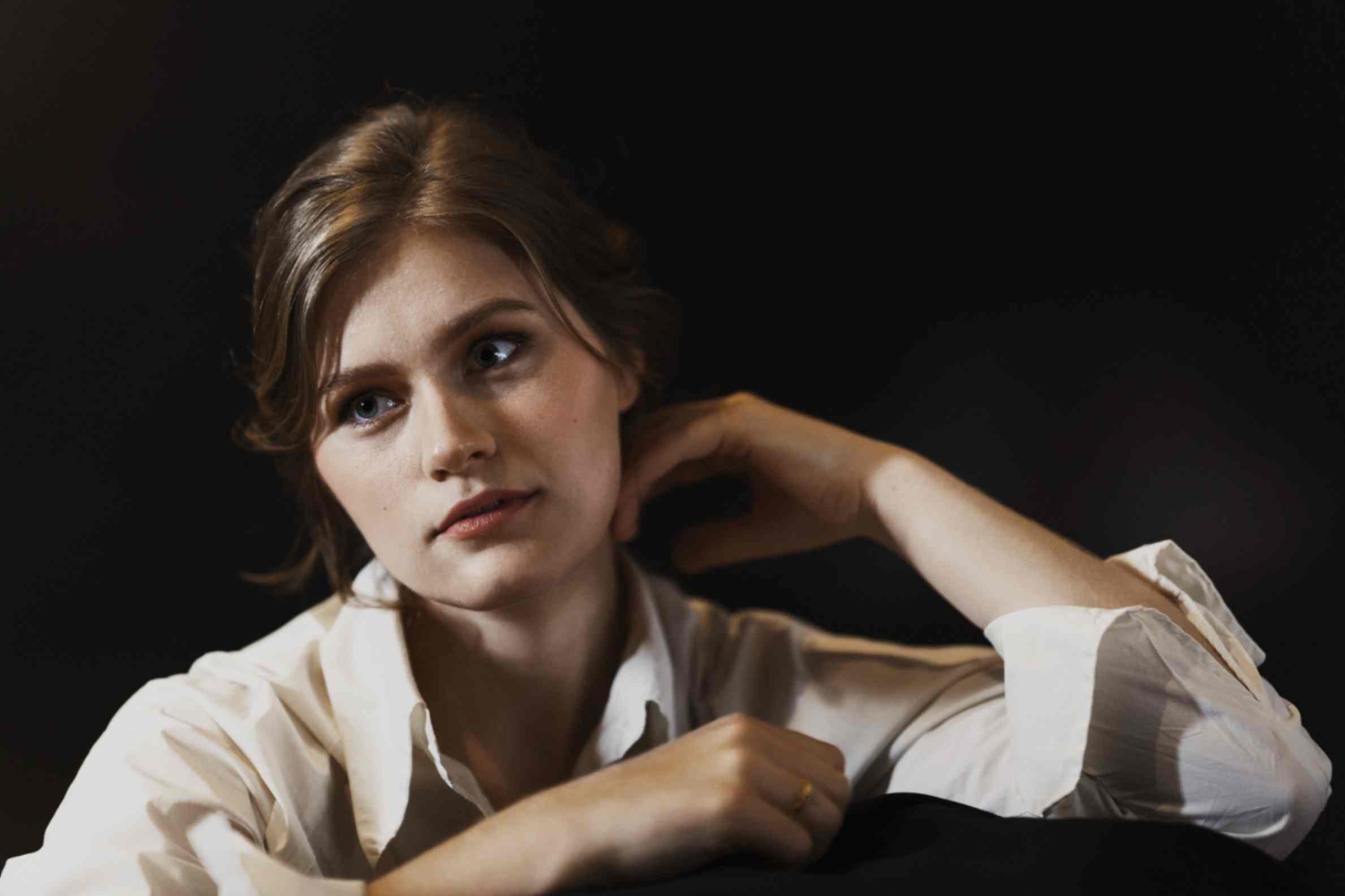 Johanna Beier, Sopranistin, in einer weißen Bluse. Den linken Ellenbogen abgesetzt und die linke Hand an den Hals gelegt.